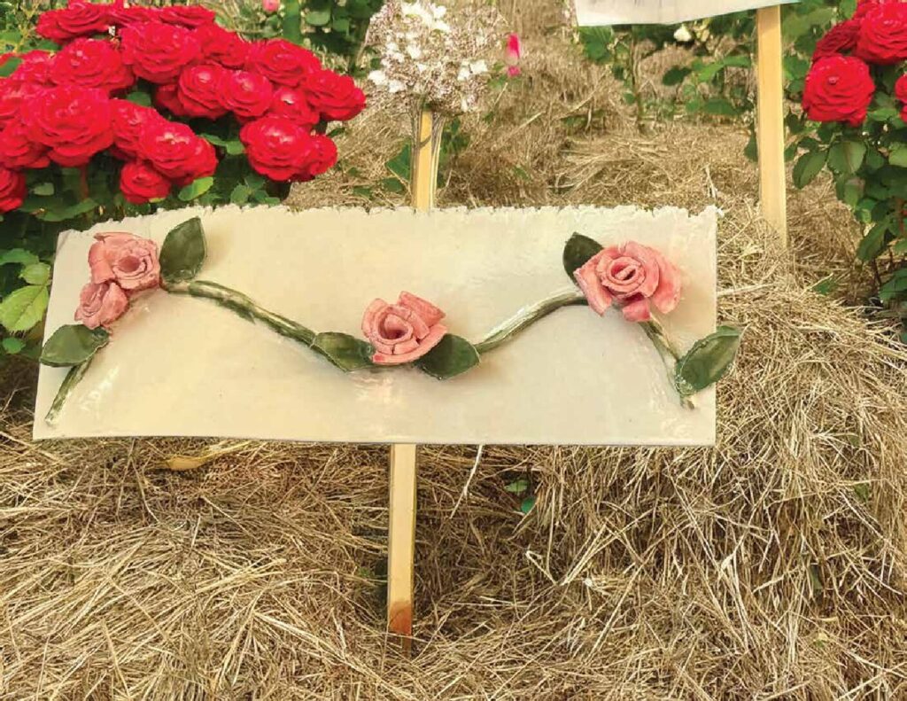 Cream clay wall hanging with a garland of sculpted pink roses and green leaves