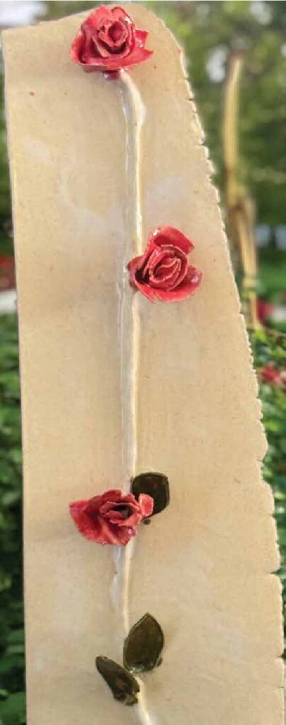 Tall cream clay wall hanging with sculpted red roses climbing a green vine