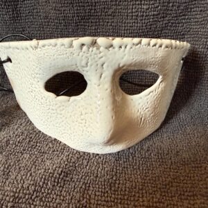 Ceramic mask in vibrant red with two eye holes, displayed against a textured gray background, highlighting its artistic craftsmanship.