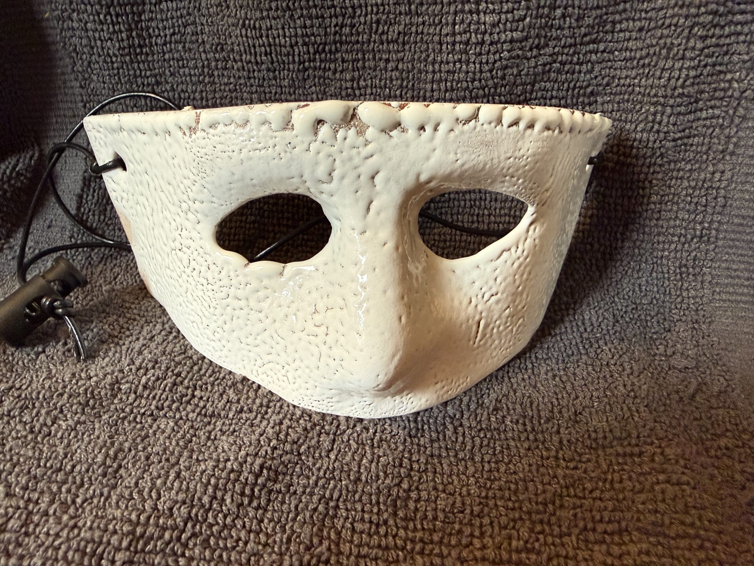 Ceramic mask in vibrant red with two eye holes, displayed against a textured gray background, highlighting its artistic craftsmanship.