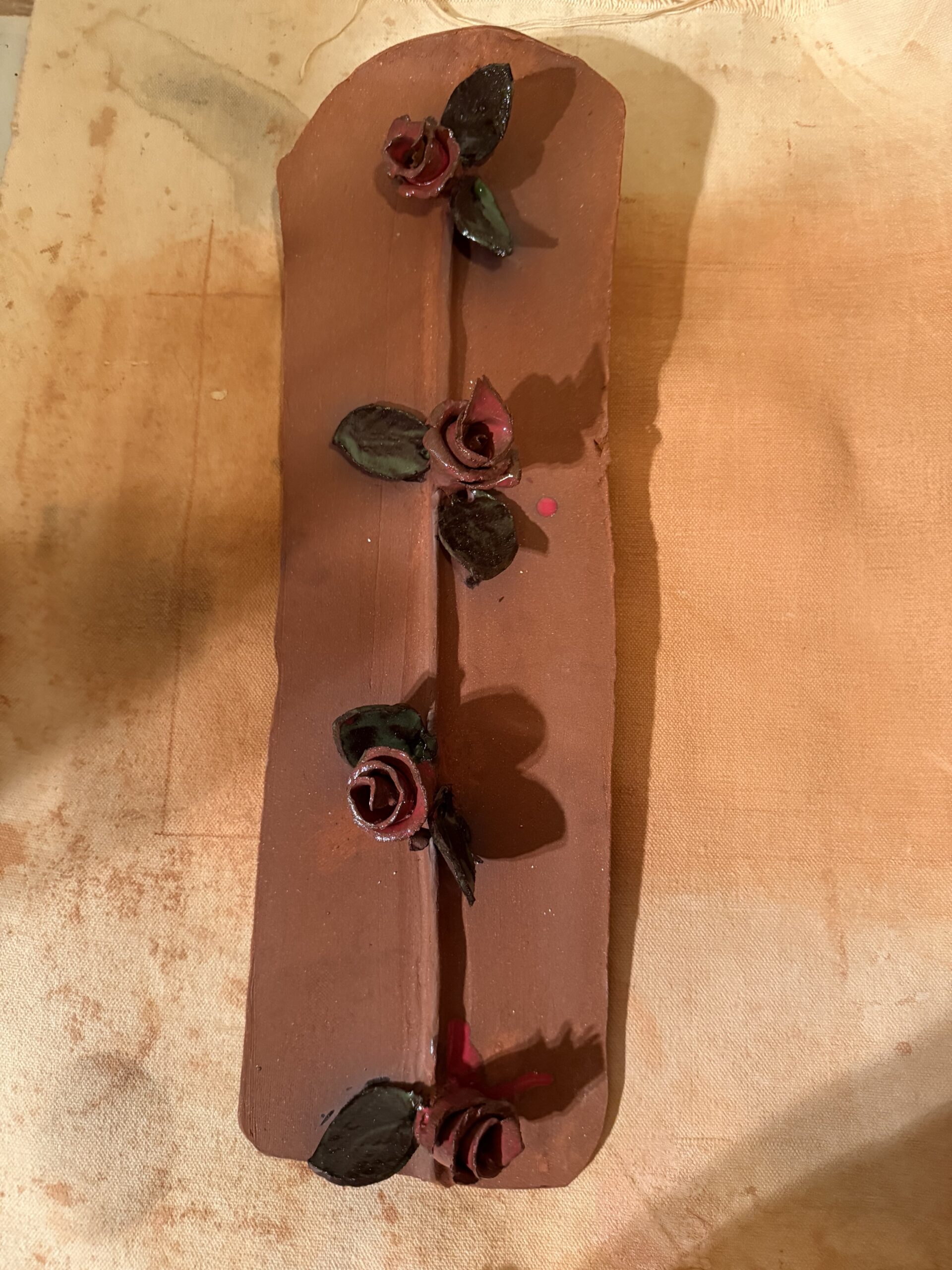 Decorative clay slab featuring four handcrafted roses with green leaves, showcasing artistic craftsmanship, ideal for pottery or art discussion.