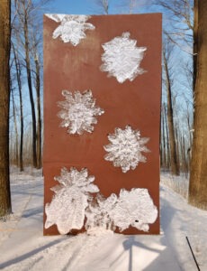 A large rust-colored panel displays intricate snowflake designs against a snowy forest backdrop, showcasing winter's beauty and artistry.