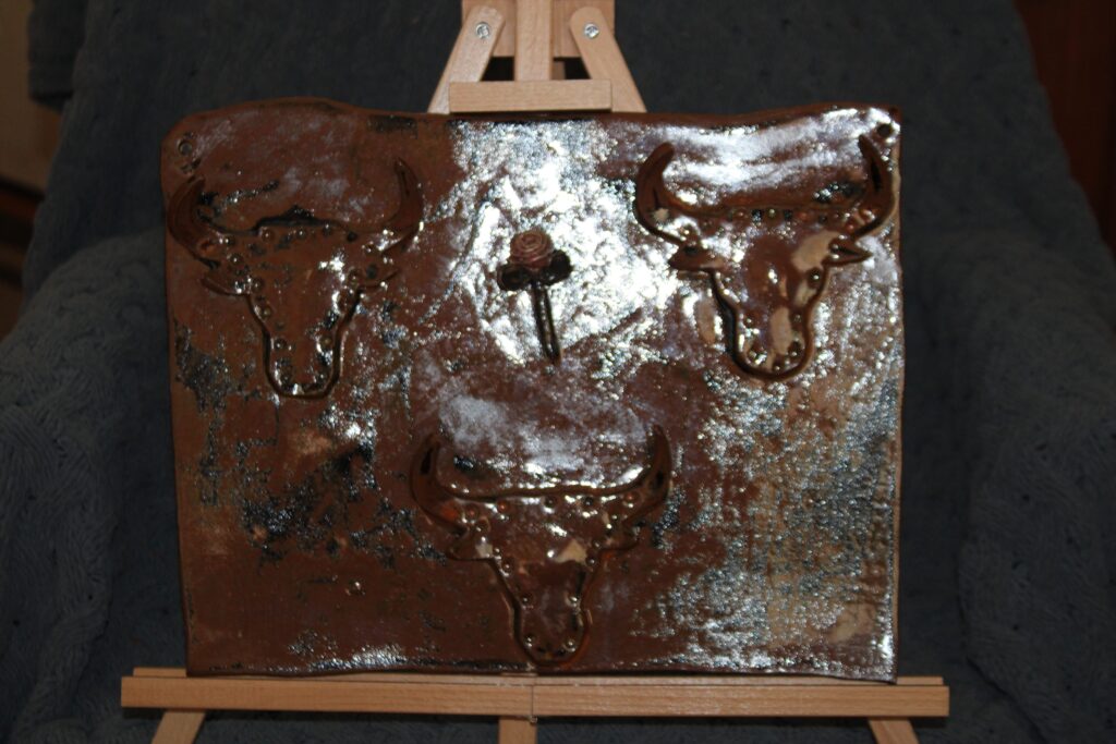 Dark brown glazed clay wall rack with two raised bull heads whose horns work as hooks