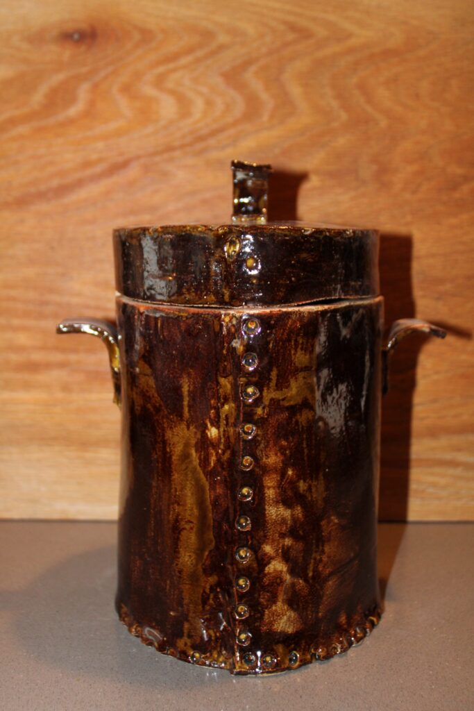 Round handmade ceramic canister with lid and side handles in an amber brown glaze