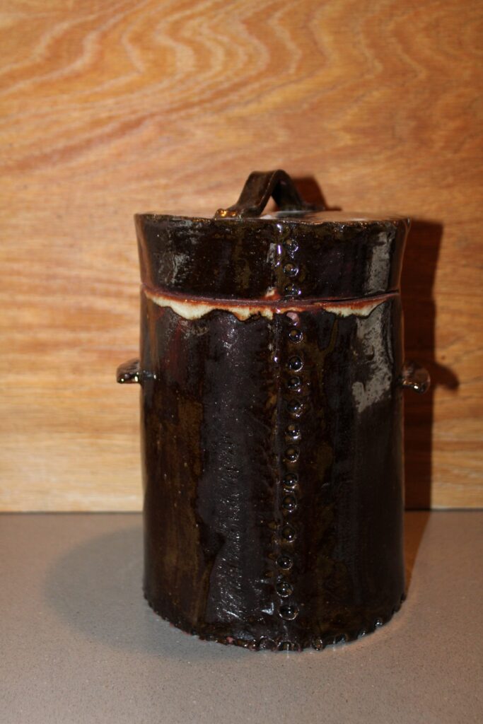 Round handmade ceramic canister with side handles in a black glaze with a cream band